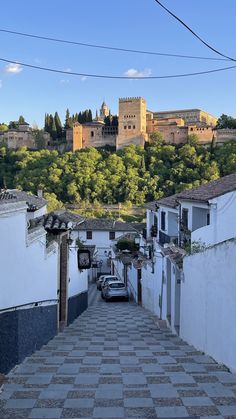 an alley way with cars parked on both sides and a castle in the back ground