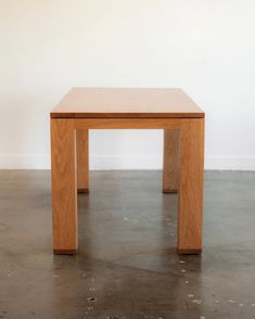 a square wooden table sitting on top of a cement floor next to a white wall