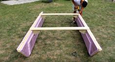 a man working on some kind of wooden structure in the middle of a yard with grass