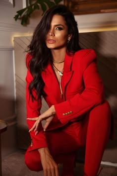 a woman in a red suit sitting on the floor with her hand on her hip