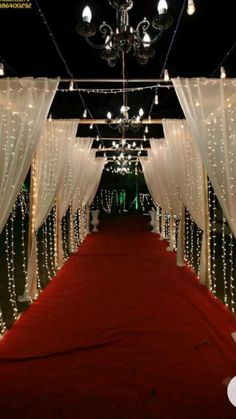 a red carpeted aisle with white drapes and lights on the ceiling is lit up by chandeliers