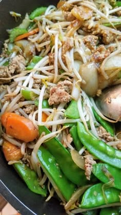 stir fry with meat, vegetables and noodles in a black bowl on a wooden table