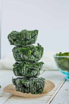 spinach chips stacked on top of each other in front of a bowl of greens