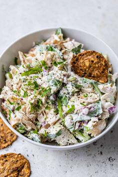 a white bowl filled with chicken salad next to crackers on the side and a cookie