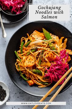 a black bowl filled with noodles and vegetables next to chopsticks