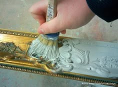 a person is using a brush to paint a gold frame