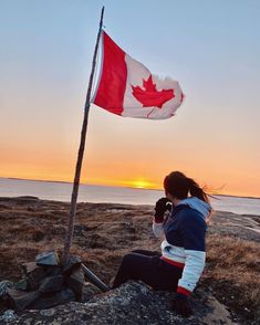 a woman sitting on top of a rock next to a canadian flag at the beach