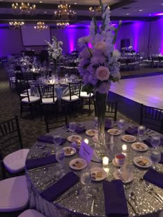 a table set up for a formal function with purple lighting and flowers in the center