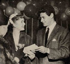 an old black and white photo of two people at a party with balloons in the background