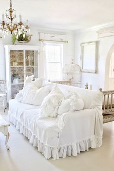 a white couch with ruffles on it in a living room next to a window