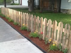 a wooden fence with flowers growing between it and a sidewalk in front of a house