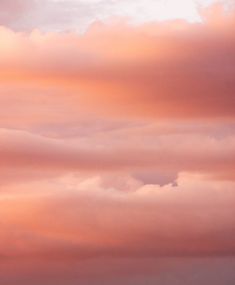 an airplane is flying in the sky with pink and orange clouds behind it on a cloudy day