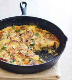 an omelet with onions and cheese in a skillet on a napkin next to a fork