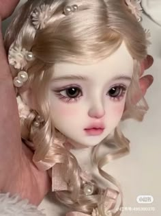 a close up of a doll with blonde hair and pearls on it's head