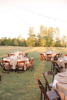 tables and chairs set up in the middle of a field with string lights strung over them