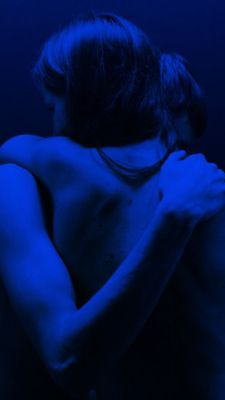 a man with his back turned to the camera in blue light, holding his hands on his chest