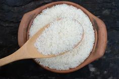 a wooden spoon in a bowl filled with white rice on top of a black surface