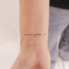 a woman's wrist with the words never give up written on her left arm