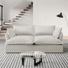 a living room with a white couch and stairs in the back ground, next to a glass coffee table