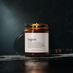 a candle that is sitting on a table in front of a dark background with the word lagom printed on it