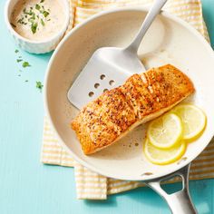 a piece of salmon on a plate with lemon wedges and a bowl of dip