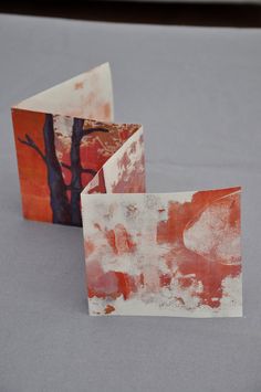 two pieces of paper with trees painted on them sitting next to each other in front of a gray background