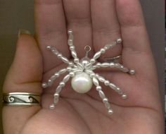 a hand holding a small white beaded spider