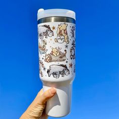 someone is holding up a cup with winnie the pooh images on it, against a blue sky