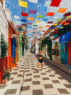 a woman is walking down the street in front of many colorful flags hanging above her head