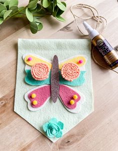 a felt butterfly is sitting on a piece of cloth next to some thread and glue