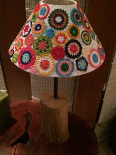 a crocheted lamp shade sitting on top of a wooden table next to a bird