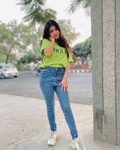 a woman in green shirt standing next to cement pillar with her hand on her hip