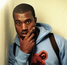 a man in a blue hoodie is holding his hand to his face and looking at the camera