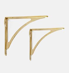 two gold metal shelf brackets against a white background, one is shaped like a triangle and the other has a curved edge