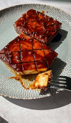 two pieces of barbecued ribs on a plate with a fork next to one another