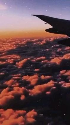 an airplane wing flying above the clouds at sunset