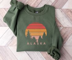 This Alaska sweatshirt is great for the Alaska lovers out there!  Also a fun shirt to wear on your upcoming Alaska cruise.  This unisex, heavy blend crewneck sweatshirt is pure comfort and will quickly become your go-to.     COLOR: This Gildan 18000 sweatshirt comes in several colors, look at the drop down for options.   SIZING: These sweatshirts are UNISEX in size.  Please check the size chart in listing photos for best fit!   MATERIAL:  -Made from polyester and cotton with a ribbed knit collar State Sweatshirts, Graphic Tees Trendy, Faith Apparel, National Park Shirt, Trendy Tees, Bachelorette Party Bride, Cowgirl Aesthetic, Mountain Shirt, Trendy T Shirts