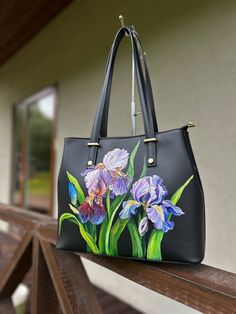 This black Cowhide leather satchel purse is hand painted. This Italy leather handbag model is perfect as a work bag for your Macbook. The Iris art leather shoulder tote bag can be a great gift for your mom, sister, or your girlfriend as well. The nice personalized wildflower messenger bag for women that will meet all her needs! Trendy, carryall, practical, and reliable to wear, this model is designed for a woman who is always on the move and needs to have all her essentials ready at hand.  The g Hand Painted Bags Handbags, Painted Leather Purse, Hand Painted Leather Bag, Painted Leather Bag, Hand Painted Purses, Painted Purse, Flower Handbag, Custom Handbags, Black Leather Satchel