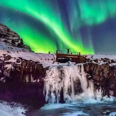 a man standing on top of a waterfall under an aurora bore