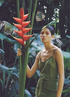 a woman standing next to a tall red flower