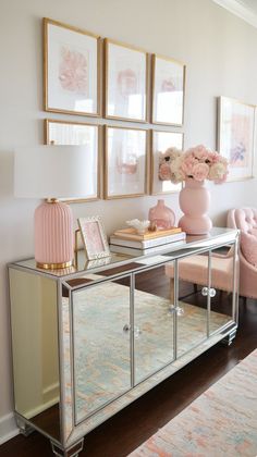 a mirrored console table with pink flowers and pictures on the wall