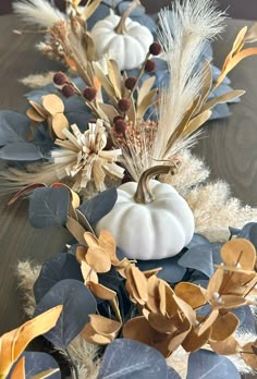 a wooden table topped with white pumpkins and blue leaves on top of it's sides