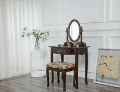 a vanity table with a mirror and stool next to a vase on a wooden floor