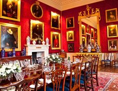 an ornate dining room with red walls and paintings on the wall, along with antique furniture