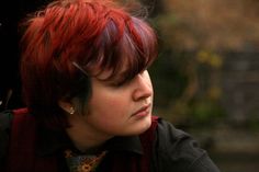 a woman with red hair wearing a black shirt and tie looking off to the side