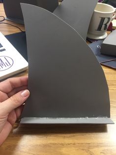 a person holding up a piece of metal on top of a wooden table next to a book