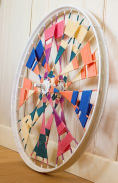 a wheel made out of strips of colored paper sitting on top of a wooden floor