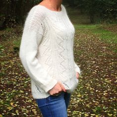 a woman standing in the woods wearing a white sweater and jeans with her hands on her hips