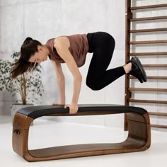 a woman is doing an exercise on a wooden bench in the middle of a room