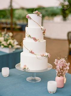 a three tiered white wedding cake with pink flowers on the top and blue table cloth